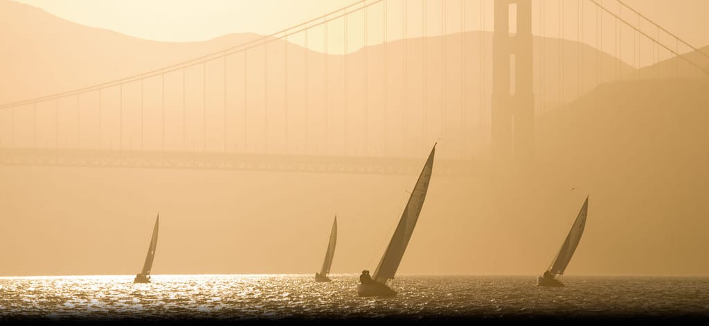 Sailboats racing on San Francisco Bay at sunset, silhouetted beneath the Golden Gate Bridge